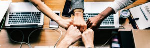 team celebrates with fist bump over desk and laptops