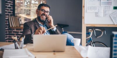 Mature business man working at modern office space, working on project. Making a call on mobile phone at his desk.  Brick wall and bicycle in  background.